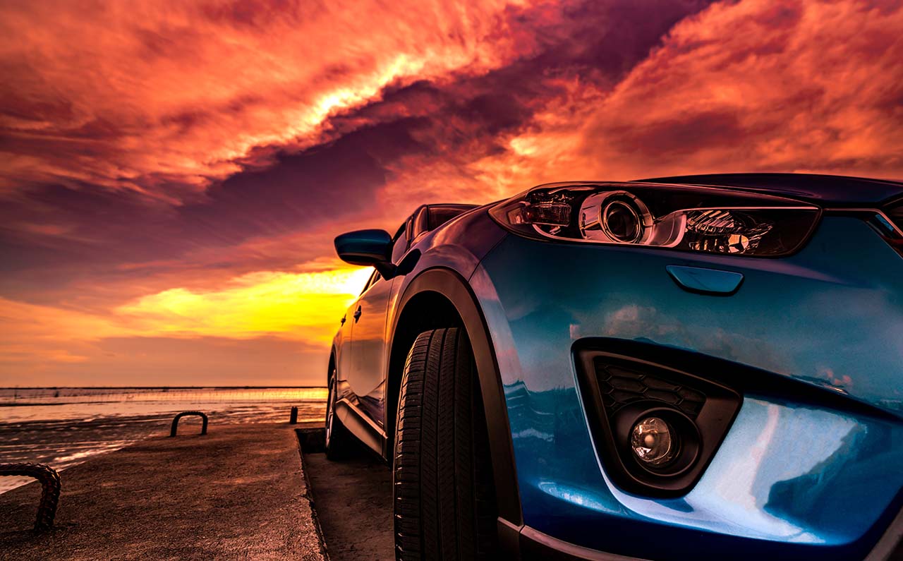 真っ赤な夕暮れが背景の青い自動車
